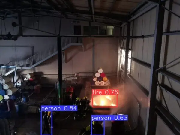 Detection overlay on a warehouse fire, labelling the flame and two people nearby with confidence scores